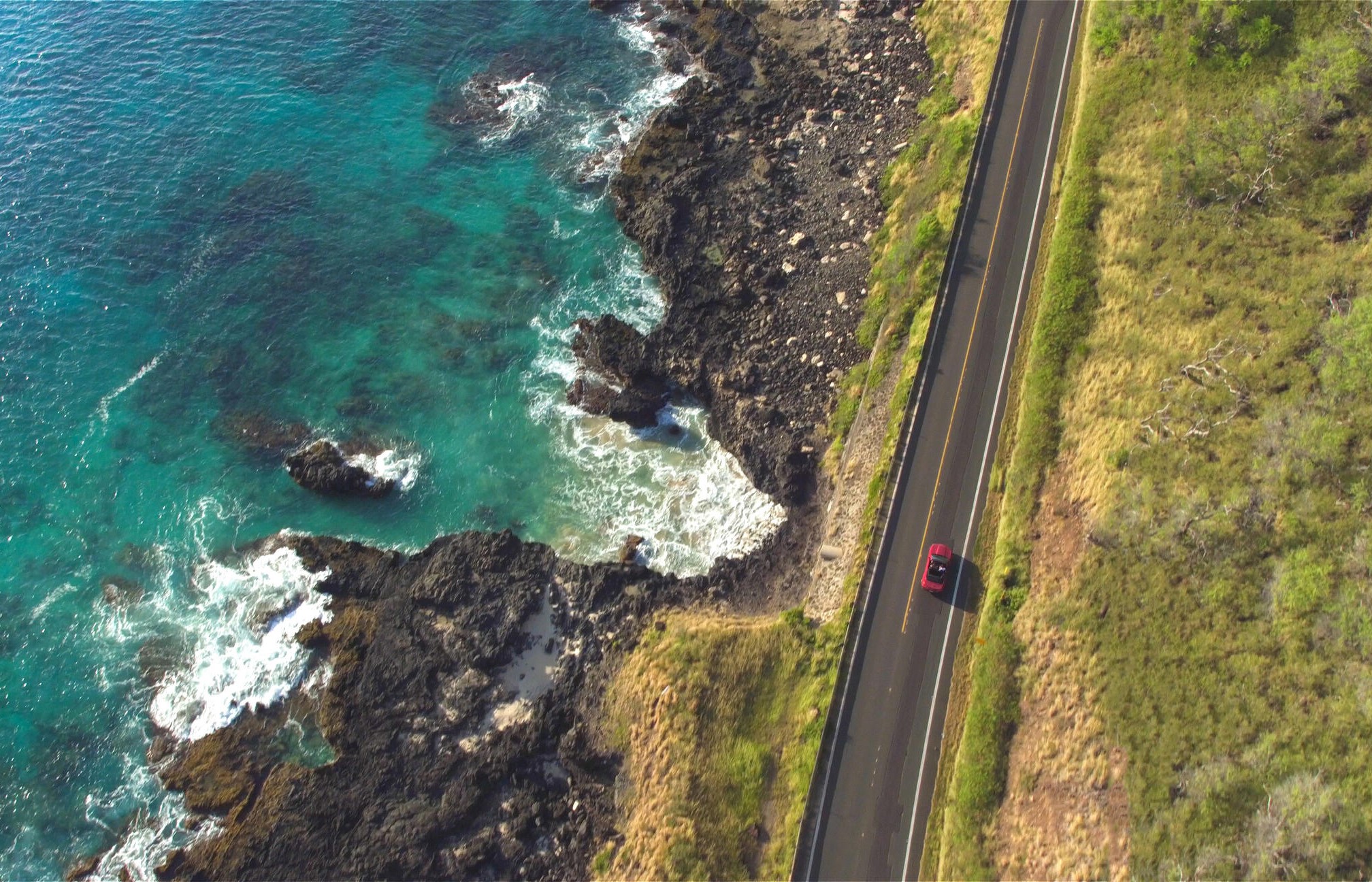 overhead view of red car driving with ocean view