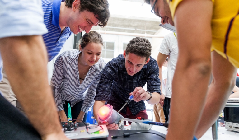 Students watch as another adjusts a light on a device.