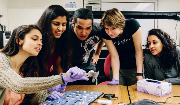 Four student watch another measure component with caliper.