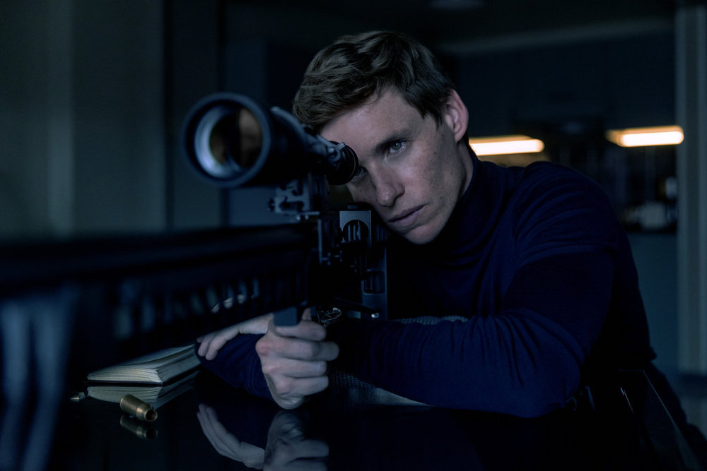 THE DAY OF THE JACKAL stars Eddie Redmayne as the Jackal, shown here wearing a blue turtleneck looking through a sniper rifle scope