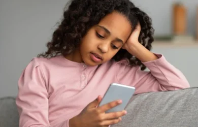 A young girl sits on the sofa looking at her smartphone.