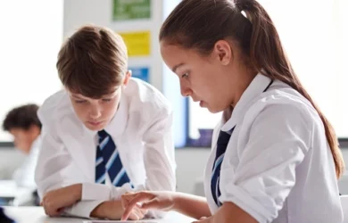 A boy and a girl in uniform, working in a classroom at school.