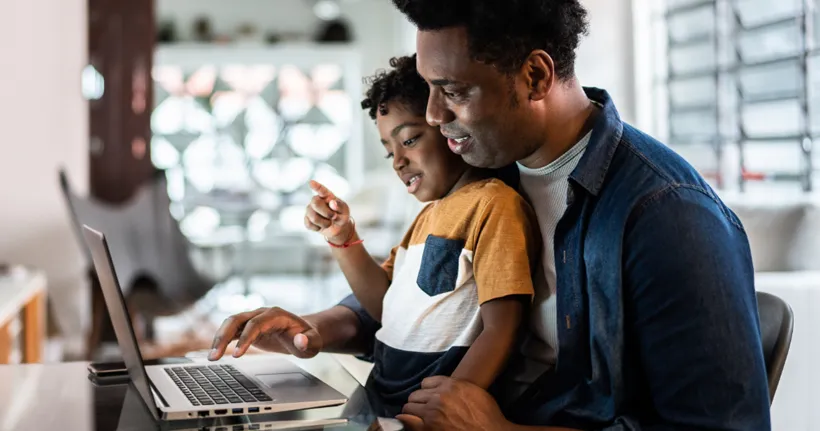 A father and his son smiling while looking at a laptop screen