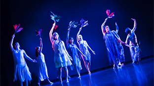 a group of women performing on stage under dark blue lights