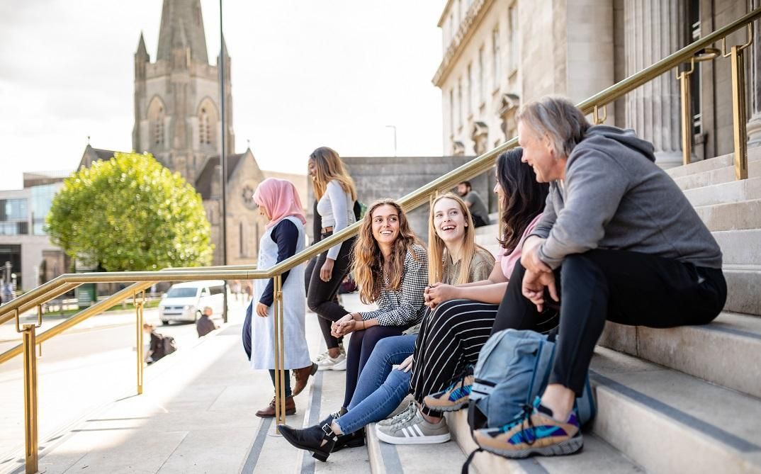 Four students sat on the Parkinson Building steps in conversation. Two students are walking past.