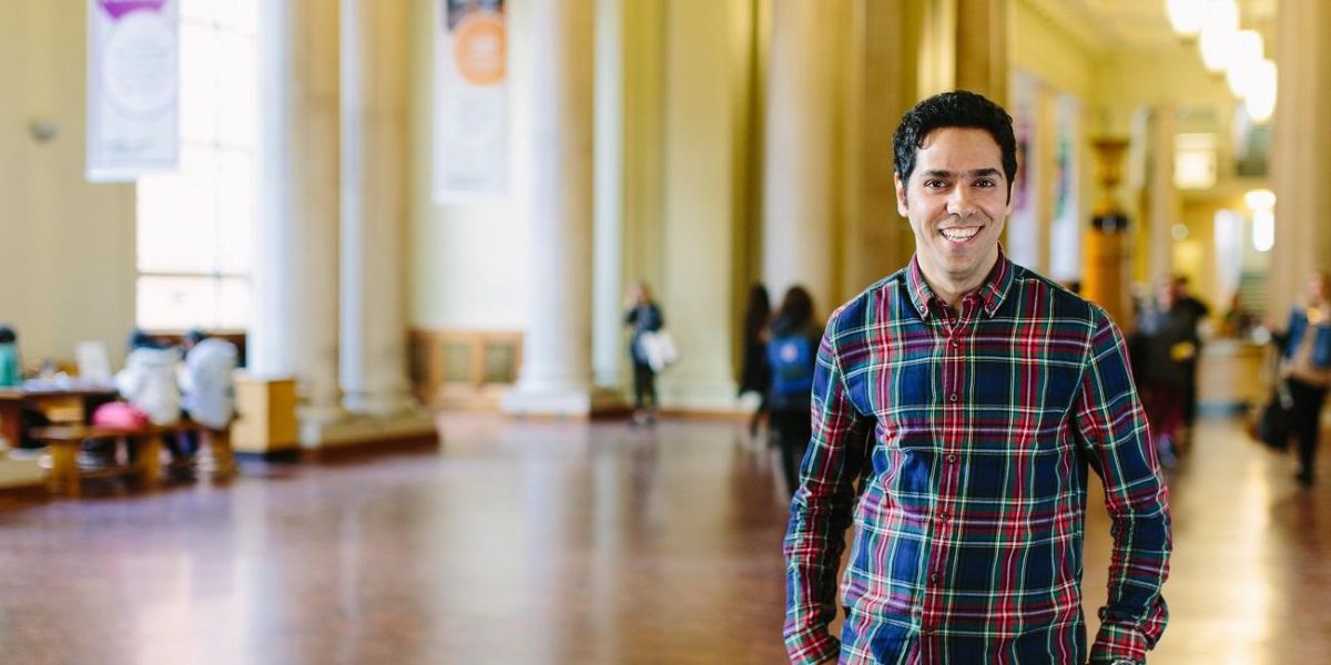 A masters student smiling and stood in Parkinson Court with people in the background