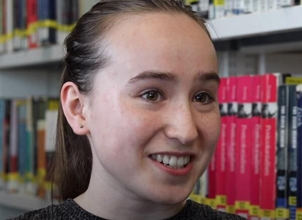 Medicine student, Penny Sucharitkul, smiling in front of a shelf of pink books.