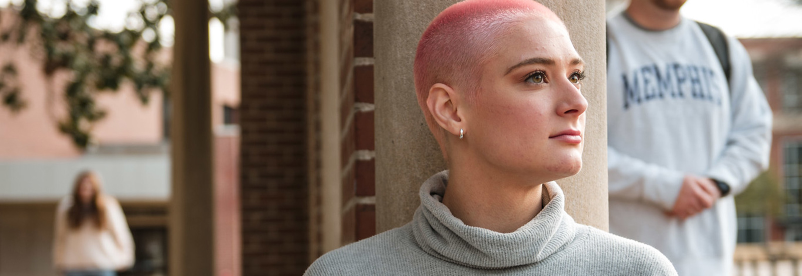 close up of student with pink hair, student with "Memphis" sweater in background