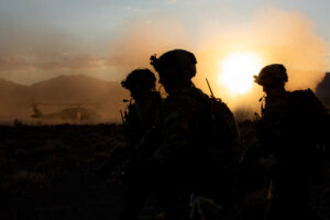 Soldiers in a field in front of a helicopter.