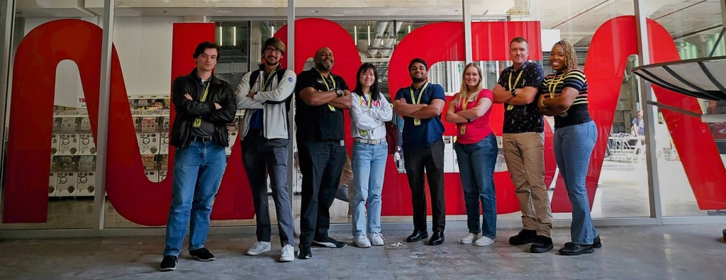 A group of students standing in front of a NASA (a/k/a NASA Worm) backdrop.