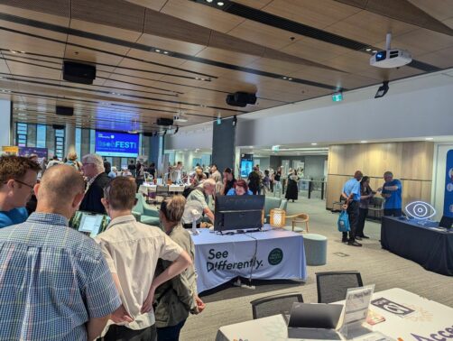 A large room with tables of exhibits and people showing off different products. A table with NVDA displays in the foreground.