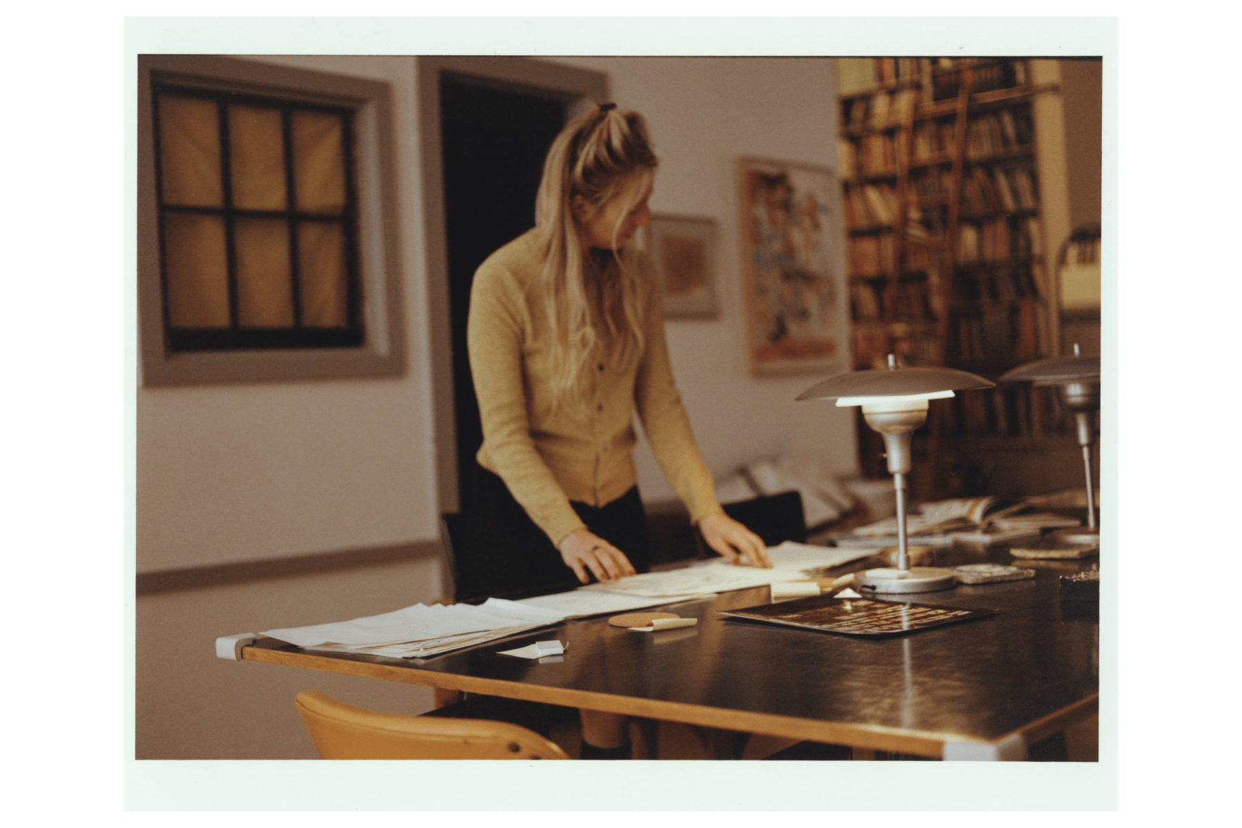 Joana Avillez stands in a warmly lit office, looking down at papers spread out on a desk in front of her.