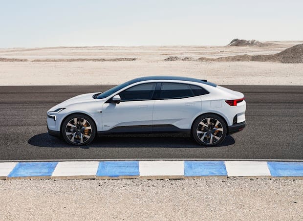 A white Polestar 4 electric SUV coupé is parked on a desert road next to a blue and white curb on a clear day.