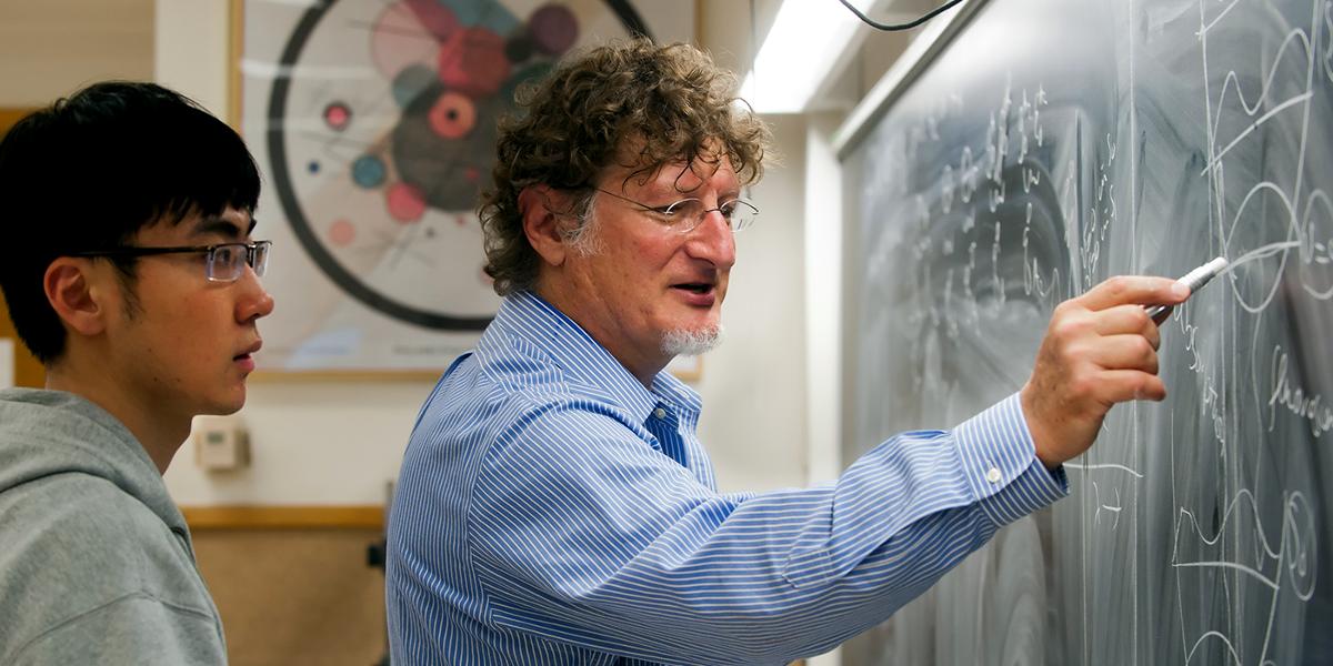 Purdue University professor writing on chalkboard with a student watching.