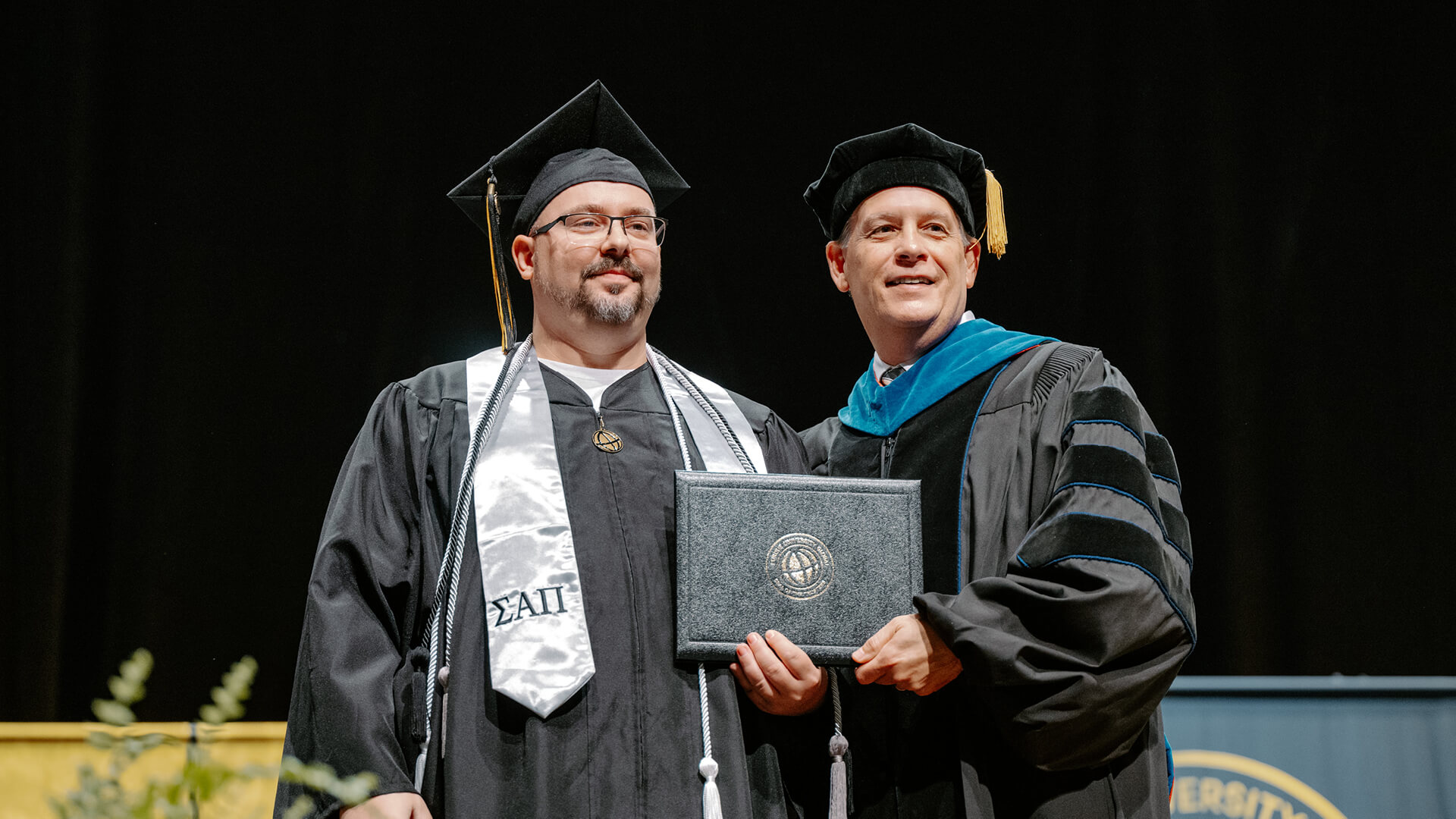 Daniel Aveline on the stage holding his bachelor’s degree.