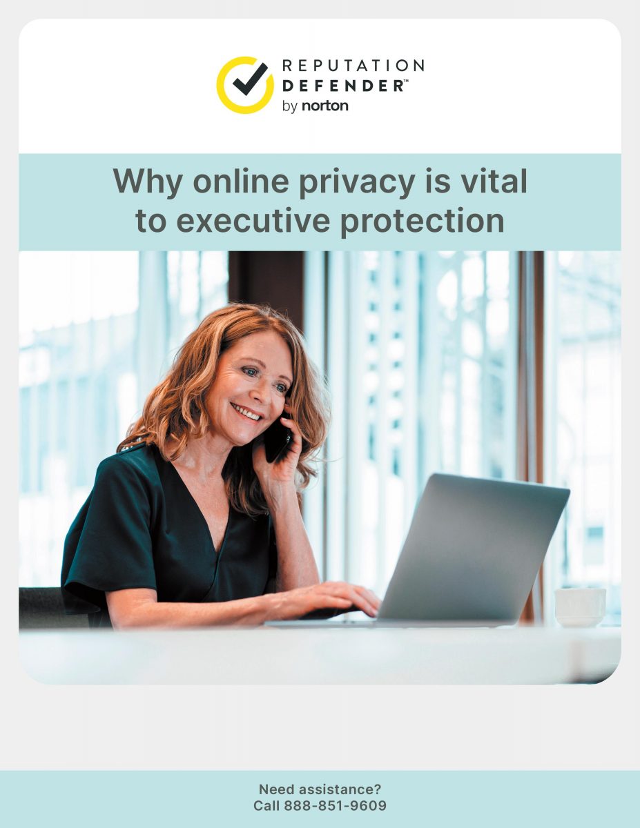 A smiling woman in a professional setting talking on the phone as she works on a laptop at a desk.