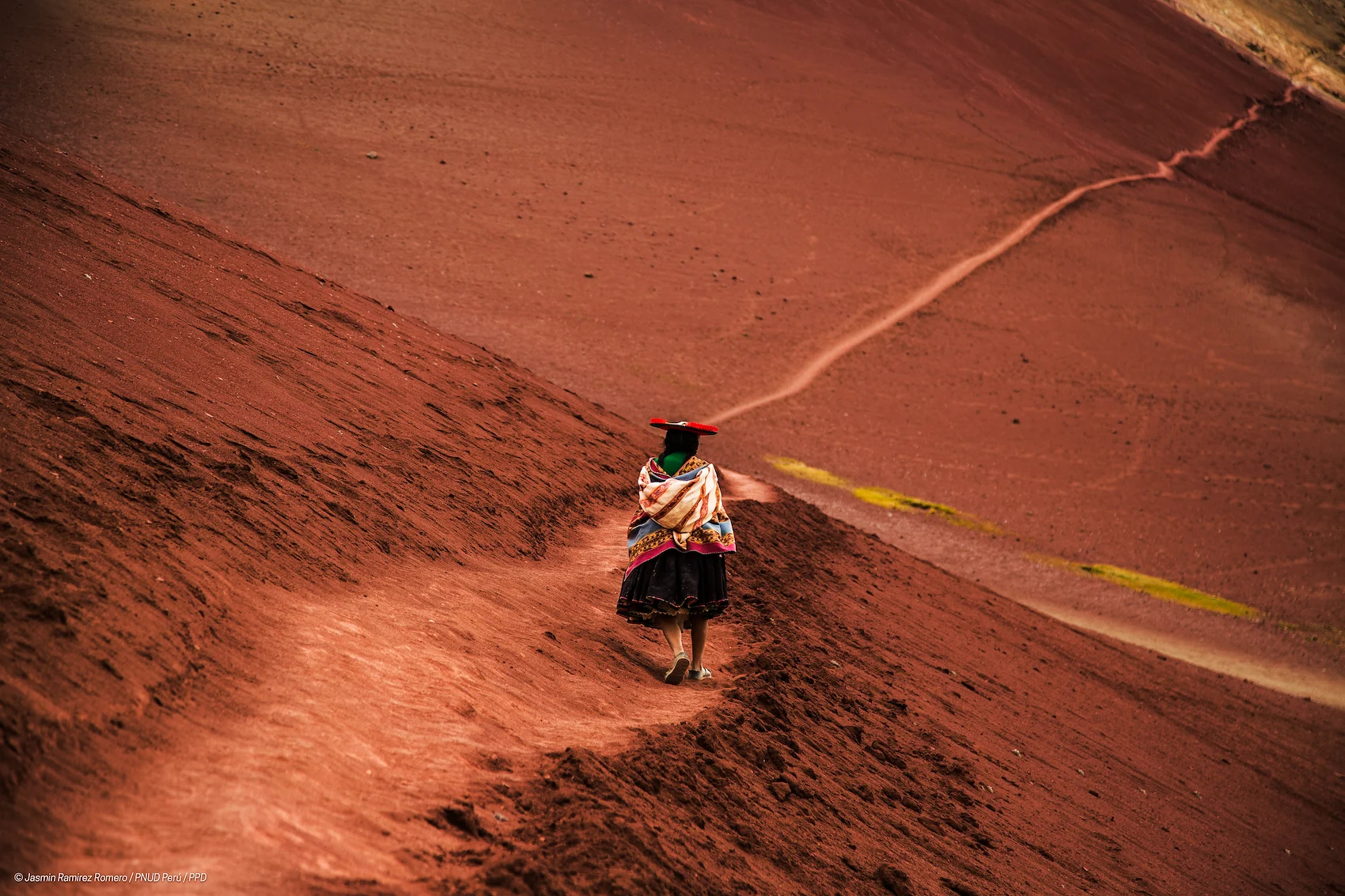 A woman in indigenous clothes walks across a sand dune