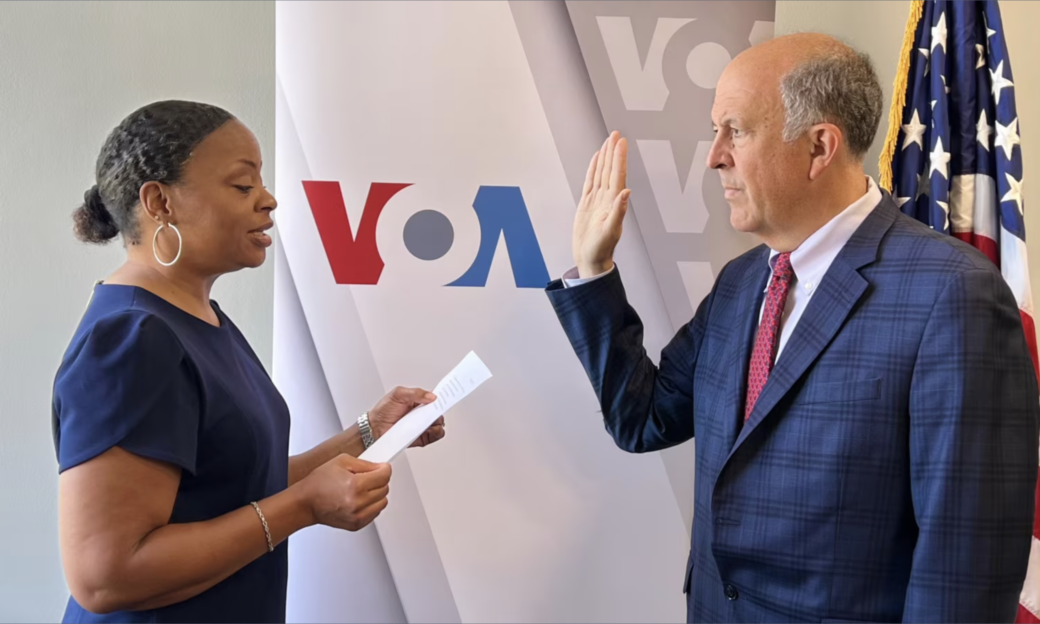 man in navy suit with his palm up and woman in navy shirt reading from a paper.