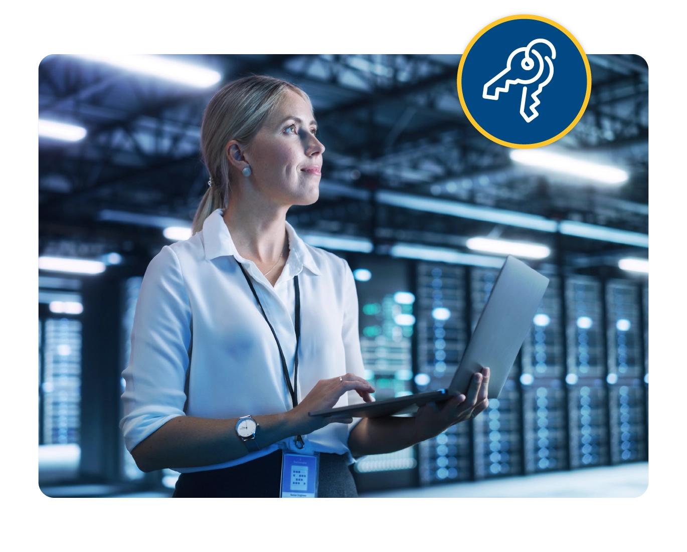 A woman stands in a data center holding a laptop. There