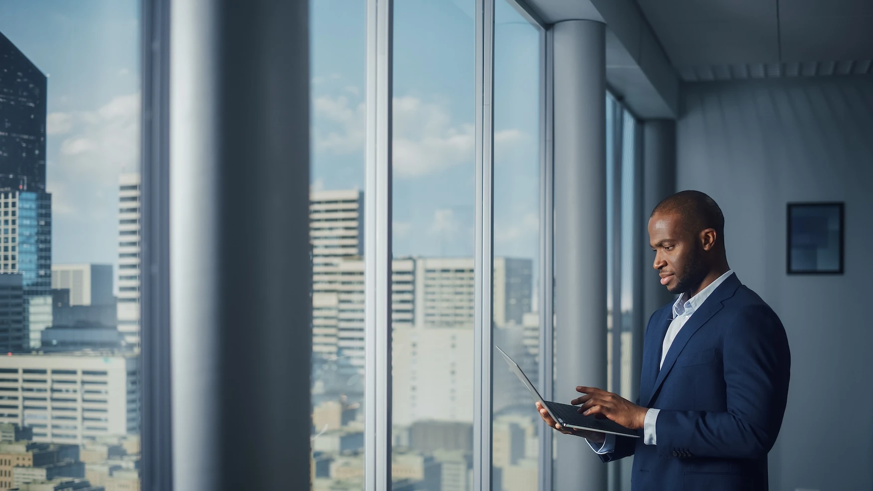 A man with a laptop looking out the window of a high-rise office