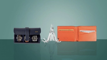 A navy, monogrammed watch roll, Leatherman multi tool and an orange wallet against a green background. 