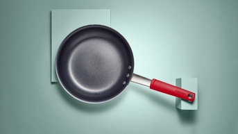 Black nonstick pan with stainless steel handle and red rubber cover on handle on a light green background.