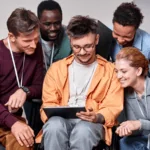 People working as a team, huddled around a young man holding a tablet.